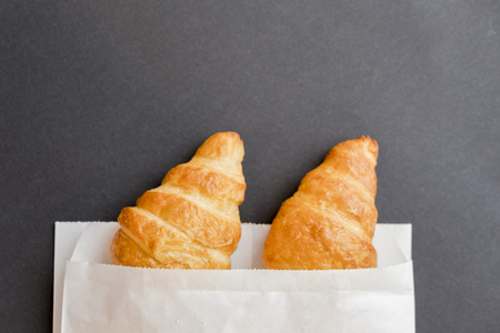 Tasty croissants in white paper bag. Rustic wooden background with sweet dessert. Top view.の写真素材