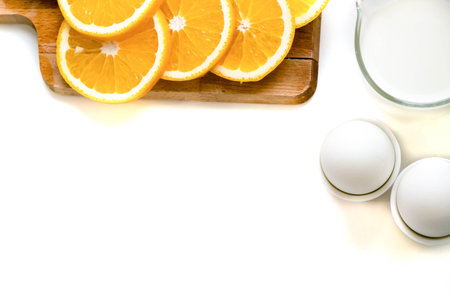 Oat flakes plate with milk, orange, eggs on a wooden white table. Top view of healthy oat flakes...
