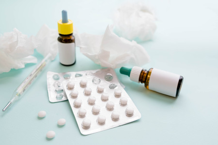 Spray for the nose or a pill to treat colds and gripes. Glass Bottle with medicines and paper handkerchiefs on a green background. Copy space for textの写真素材
