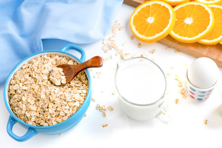 Oat flakes plate with milk, orange, eggs on a wooden white table. Top view of healthy oat flakes breakfast. Copy space. blue napkin Breakfast in bed plate, breakfast table buffet. Healthy ingredientsの写真素材