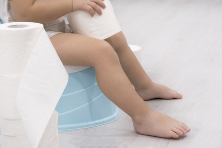 smiling baby sitting on chamber pot with toilet paper rollsの写真素材