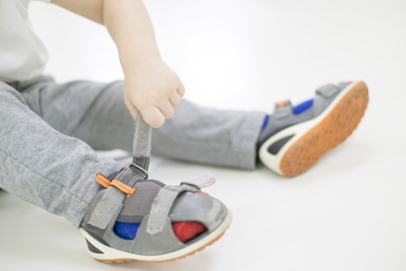 Small child tries to put on his shoes. Baby boy with shoes in hand isolated on white.の写真素材