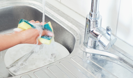 Cropped image of attractive young woman is washing dishes while doing cleaning at homeの写真素材