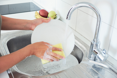 Cropped image of attractive young woman is washing dishes while doing cleaning at homeの写真素材