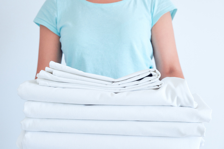 housewife holding a stack of washed bed linen. washing clothes and linen, bleaching of white thingsの写真素材