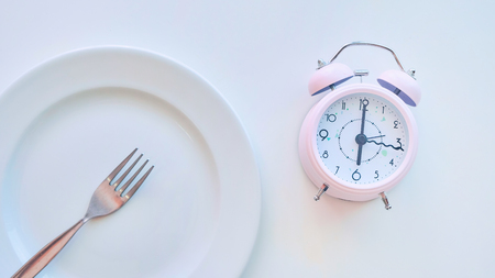 clock on an empty plate, white background. the concept of limiting the intake of food.の写真素材