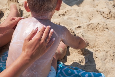 mother is putting on boy back a sunscreen on the beachの写真素材