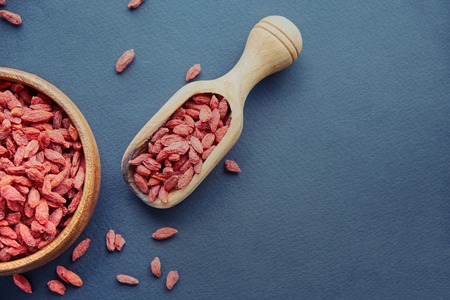 Goji in bowl on wood table. Top view of fresh goji in scoop and bowl. Goji in heart shape on table.の写真素材