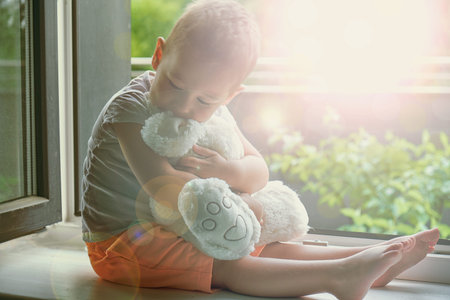 boy of two years sitting by the window and hugs a toy Bunny. rainy weather, waiting for dad to come...