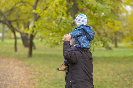 Happy weekend concept. happy grandfather and grandson are walking in the park. Autumn day. Grandpa rolls on the shoulders of a little boy.の写真素材