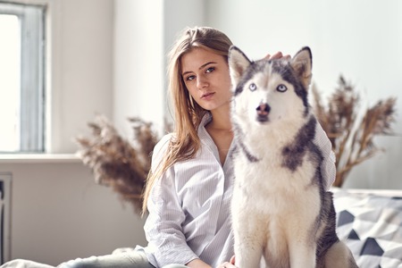 blonde girl playing with her dog husky at home.の写真素材