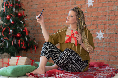 happy young beautiful girl talking on the phone or taking a selfie with her gift. shopping for christmas. uses the smartphone to write a thank you message for the gift.の写真素材