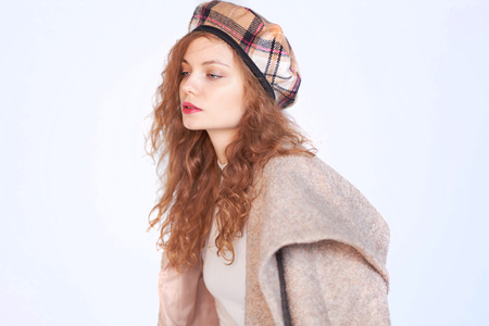 Beautiful girl dressed in french style on a white background. red hair woman is wrapped in a coat, winter clothes. Smiling lady wearing warm clothes, winter portraitの写真素材