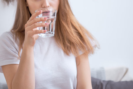 woman drinking water in the morning at home. detox concept, health care. blonde in a white T-shirt...