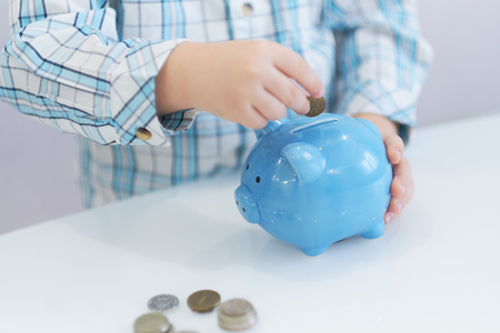 three years old boy puts money in a piggy bank, piggybank concept. mantesori space in the houseの写真素材