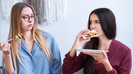 two girls eat their lunch, a woman on a diet, refuse junk food and eat salad. care about the health, nutrition of students.の写真素材