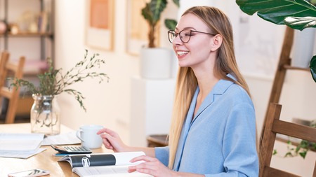 Young beautiful woman with long disheveled hair, wearing glasses, working in the office, happy smileの写真素材