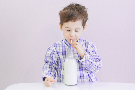 cute happy boy with dark eyes drinks milk from a bottle. the child is wearing a plaid shirtの写真素材