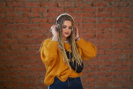 Nice young girl in headphones laughing looking at camera over Brick wall background.