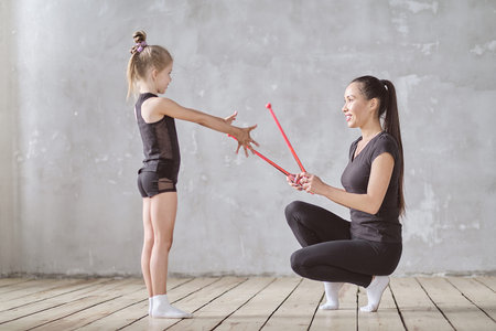 Graceful little girl ballerina standing on hands and stretching with teacher in dance studio