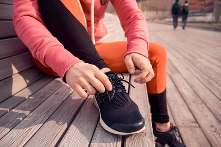 Unrecognizable young runner tying her shoelaces. Studio shot on wooden floor background.の写真素材