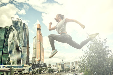 Young woman with fit body jumping and running. Female model in sportswear exercising outdoors.
