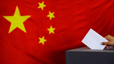 Hand holding ballot paper for election vote concept. elections, The hand of woman putting her vote in the ballot box. China Flag on background.の写真素材