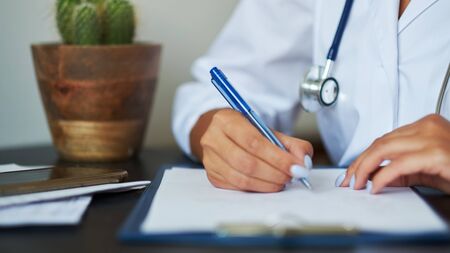 Young therapist filling medical checklist sitting at the desk. Health care and insurance concept. Female doctor doing paperwork in the office.の写真素材