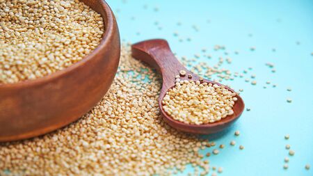 White quinoa seeds on a blue background. quinoa in bowl and a spoon on kitchen table top view. Healthy and diet superfood product.の写真素材