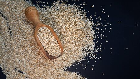 White quinoa seeds on a black background. quinoa in spoon on kitchen table top view. Healthy and diet super food product.の写真素材