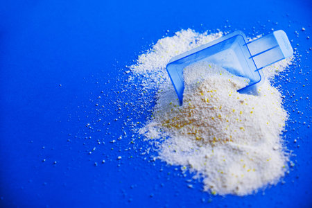 Measuring scoop with laundry powder on multi-colored background.
