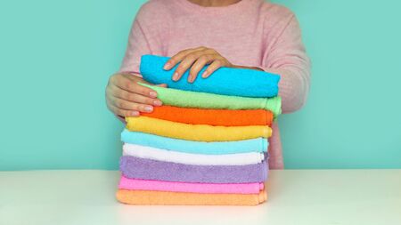 Close-up of hands putting stack of fresh bath towels. multi-colored rolls of towels in a wicker basket on a blue background.の写真素材
