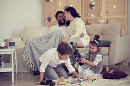 little boy girl having fun, friendship between siblings, family leisure time in living room. Children sister and brother playing drawing together on floor while young parents relaxing at home on sofaの写真素材