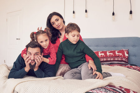 Young family with two kids at home in bed. Parents with children relaxing in bed on a sunny morning....