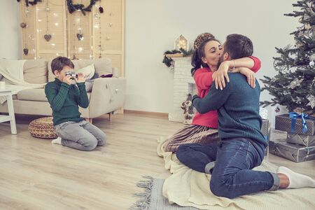 son takes pictures of dad and mom. couple posing under christmas tree for photographer s sonの写真素材