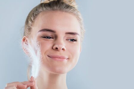 Portrait of attractive girl with closed eyes. beautiful woman with a white feather near her face. Face and body skin care concept, fresh clean shiny skin.の写真素材
