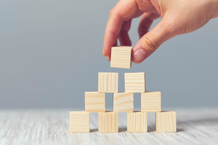 Hand arranging wood cube stacking as step stair. Business concept growth success process on blue...