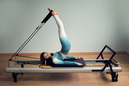 young asian woman pilates stretching sport in reformer bed instructor girl in a studio
