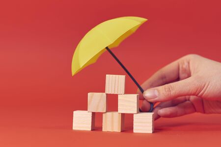 wooden blocks under umbrella on table against red background.の写真素材