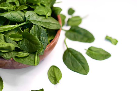 Fresh spinach in a wooden bowl isolated on white background.