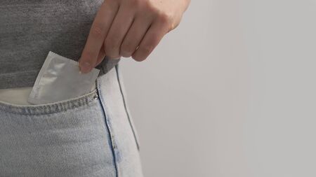 Condom in the pocket of blue jeans. Girl puts hand condom in the pocket of blue jeans. Close up.の写真素材