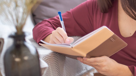 Close up partial portrait female author at home writing in journal
