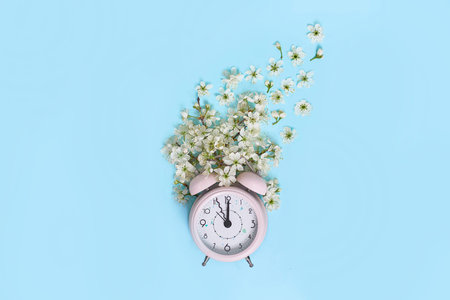 Pink alarm clock and delicate little white flowers on blue background. Top view. Time for love and...