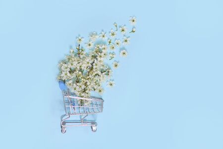 flowers fly out of the shopping cart on a blue background. spring shopping concept. seasonal sale.の写真素材