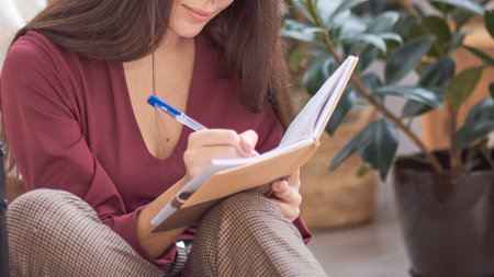 Close up partial portrait female author at home writing in journal