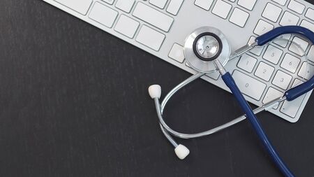 Silver stethoscope lying down on white keyboard, on black background. stock image photo. remote diagnosticsの写真素材