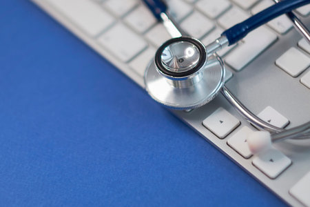 Silver stethoscope lying down on white keyboard, toned blue. stock image photo.