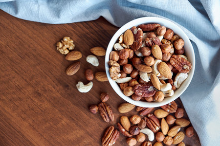 Wooden bowl with mixed nuts on table top view. Healthy food and snack. Walnut, pistachios, almonds,...
