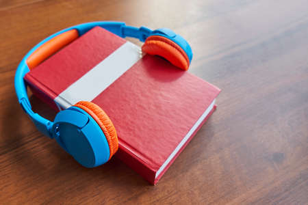 Audio book concept. Headphones and red book on a wooden table. Top view with space for your text. Flat lay, top view, copy spaceの写真素材