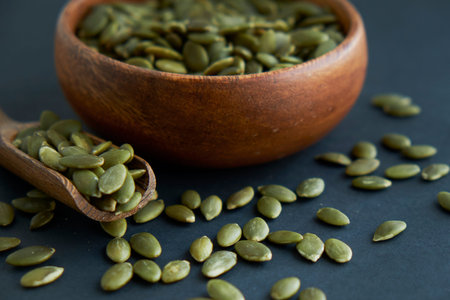 pumpkin seeds in a wooden bowl and vintage scoop. Close up on a black background. copy space for...